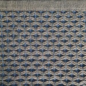 Et håndvevd teppe med en tydelig strukturert overflate. Teppet har en levende melering og en diskret kantavslutning