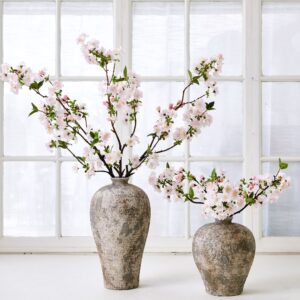 Naturtro gren av kirsebærblomst i silke med hvite og rosa blomster og små grønne blader.